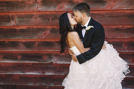 Bride envelopes groom in her curly dress while he kisses her tenderの写真素材