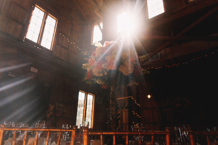 Bright rays of daylight shine from the high windows in wooden hangar prepared for a wedding dinner