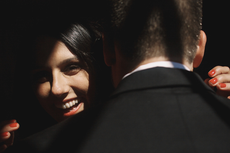 Brunette woman smiles in the ray of light over man's shoulderの写真素材