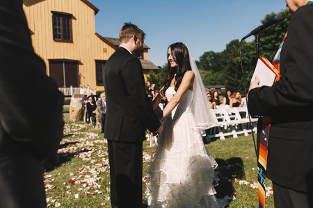 Groom admires beautiful bride while holding her hands during the ceremonyの写真素材