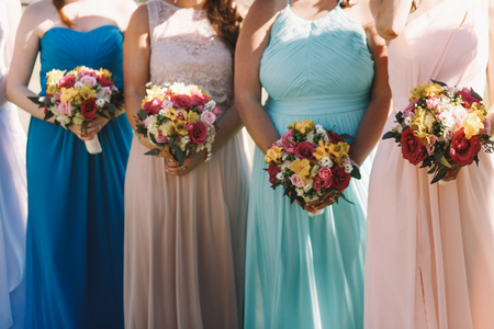 Bridesmiads in pastel dresses hold wedding bouquets in their hands while standing outsideの写真素材