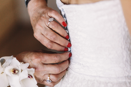 Hands of old woman buttons up a corset on the brideの写真素材