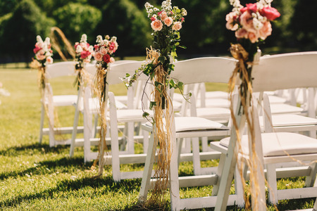 Ropes which hold pink bouquets on white chairs hang from themの写真素材