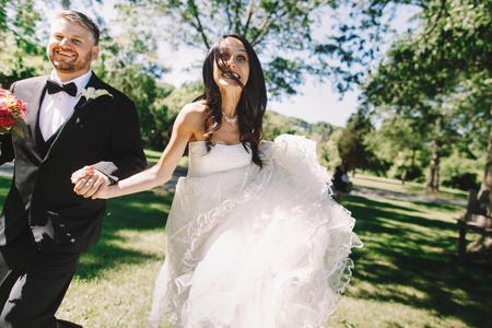 Bride looks funny running together with a groom in black tuxedoの写真素材