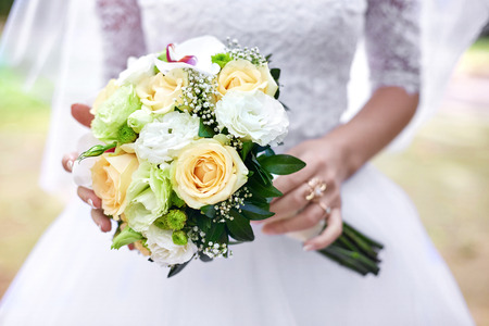 Bride's delicate hands hold gorgeous bouquet of white and beige rosesの写真素材