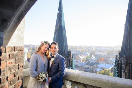 Attractive groom and bride in grey jacket stand on the balcony with great view on the cityの写真素材