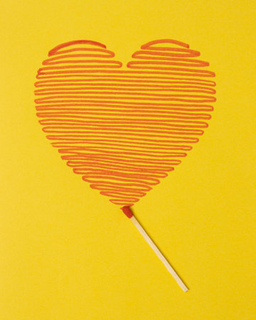 Red heart drawn with a match on a yellow background. Minimalistic scene for Valentine`s day.の写真素材