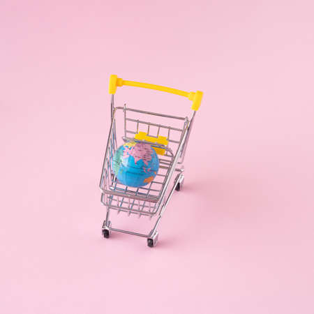 Geographical globe in a supermarket cart. Minimalist concept on pink background.の写真素材