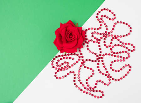 Red necklace and rose on a green-white background. Minimalistic concept with place for message.の写真素材