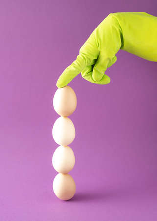 Four eggs arranged vertically are held by a hand in a green glove. Easter decoration on  purple background.の写真素材