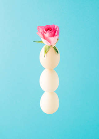 Three eggs vertically arranged and a pink rose on top. Minimal Easter arrangement on bright blue backgroundの写真素材