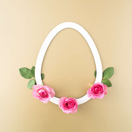 White egg shape frame decorated with pink roses  on a golden background. Creative concept for Easter.の写真素材