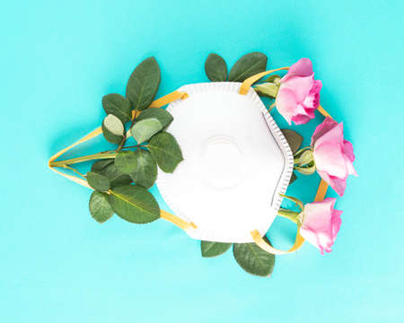 Three pink roses covered with a medical mask on cyan background.  Minimal  conceptの写真素材