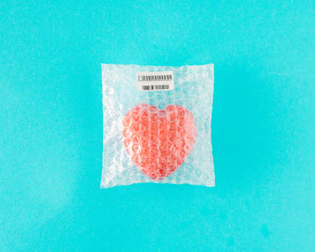 Red heart wrapped in a bag for fragile items. Minimal emotional concept on a light blue background.
