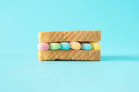 Colorful soft gummy candie between two pieces of toast . Light blue background.