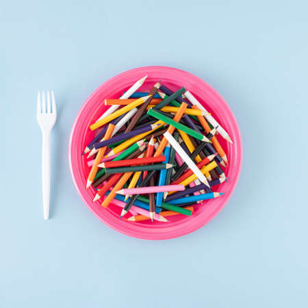 A pink plate full of wooden crayons and a white fork next to it. Minimal concept on a blue...