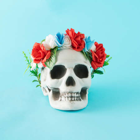Beautiful fresh flower wreath on human skull.  Minimal Halloween concept on a blue backgroundの写真素材