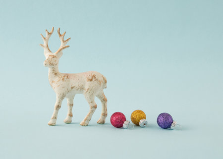 Red, purple and gold Christmas ball next to a white deer with brown patterns. Minimal New Year's concept on a blue backgroundの写真素材