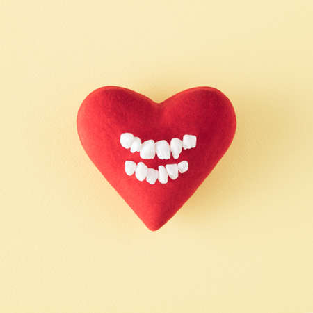 Big red heart with white teeth in the middle. Minimalist funy concept of love on a pastel yellow...