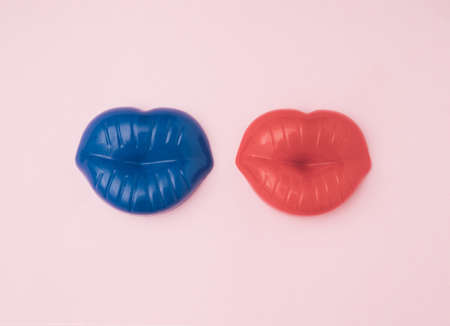 Blue and red lips next to each other on a light pink background. The minimal concept of a couple in...