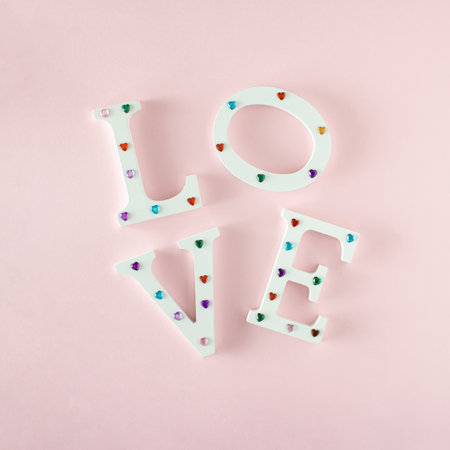 The word love is written in white letters that are decorated with colorful hearts and arranged on a pastel pink background. minimal concept of loveの写真素材