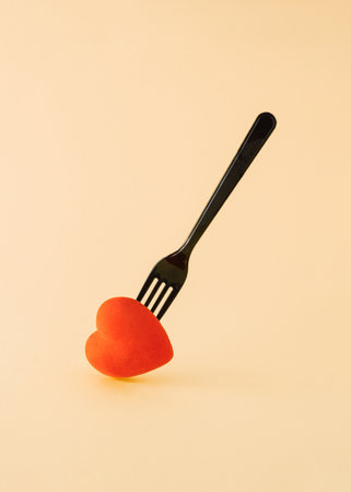A red heart pierced with a black fork. Minimal concept on pastel yellow backgrounds. A symbol of loveの写真素材