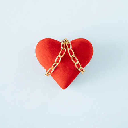 Red heart tied with gold chains. Minimal concept of love. Light blue backgroundの写真素材