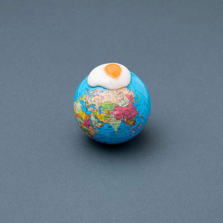 Fried sunny-side-up egg on the globe. The minimal concept of a hot planet. Black background