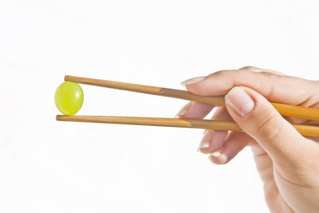Beautiful hand of a woman holding a green grape with chinese sticks against white background.の写真素材
