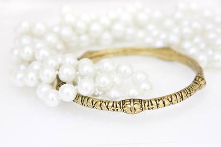 Set of brass bracelet and a lace of imitation perals on white.の写真素材