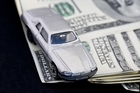 Silver toy car over hundred dollar bills against black background.