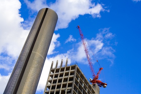 Skycraper building site with red construction crane against dramatic cloudscape.の写真素材