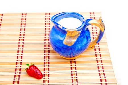 Milk jar and single strawberry on straw matの写真素材