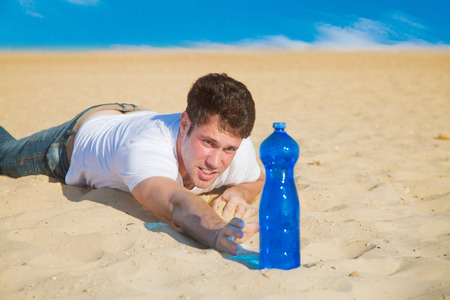Young man crowling to a bottle of water in the middle of desertの写真素材