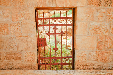 Old rusty barred door with a Christian cross in a pink limestone wallの写真素材
