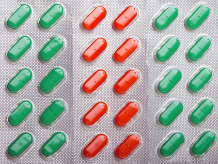 Background of orange-red and green pills in silver blisters