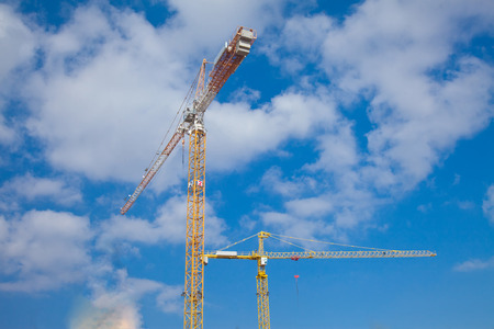 Two yellow construction cranes against beautiful blue sky with cloudsの写真素材