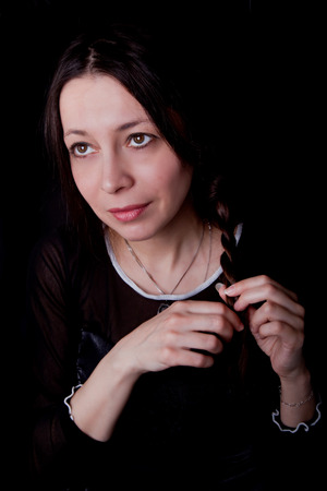 Woman with a tender smile braiding her hair (classic portrait on black background)の写真素材