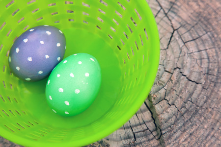 Two dotted Easter eggs in a plastic basket sitting on a wood stumpの写真素材