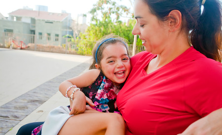 Little girl laughing happily in her mother's lap (sunset lighting)の写真素材