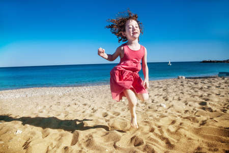 Cute little girl jumping happily with her eyes closed at seasideの写真素材