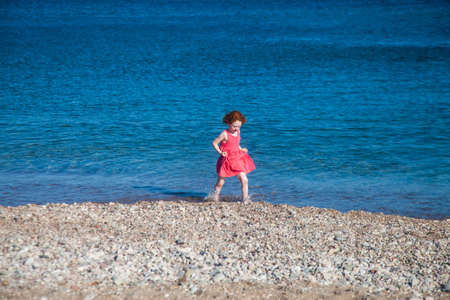 Cute redhead girl walking the sea shore holding her pink dressの写真素材