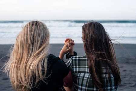Two young girls from the back join their hands sitting in front of the sea. LGBT conceptの写真素材