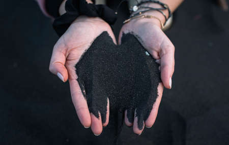 Hands of a Caucasian woman picking up black sand from a beachの写真素材