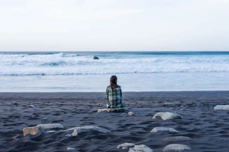 Dark-haired girl seen from behind looking at the sea. Strong waves in the Atlantic Oceanの写真素材