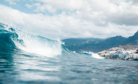 Low angle of a breaking wave on a cloudy day with buildings in the background. Playa de las...
