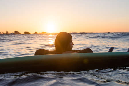 Surfer girl waiting for a wave in the water at sunsetの写真素材