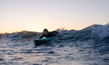 Low angle view of a surfer girl catching a wave. Paddling on a board in the waterの写真素材