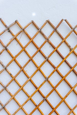 Grid of wooden fence isolated against old white wall background. Closeup.の写真素材