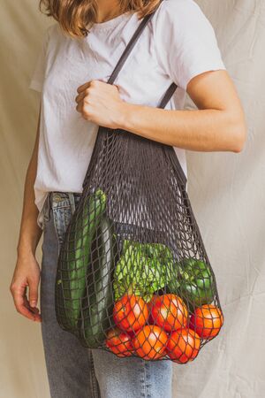 Girl holding mesh shopping bag with vegetables. Sustainable, zero waste and plastic free lifestyle.の写真素材